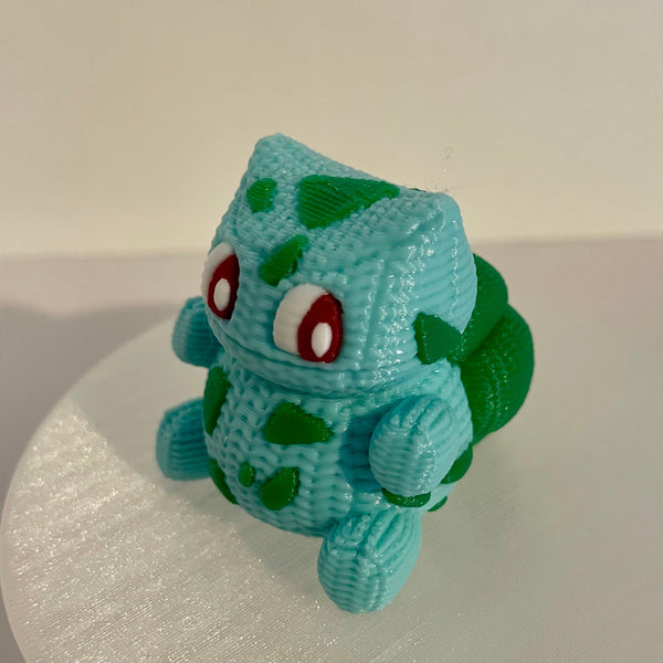 Handmade knitted-style 3D printed Pokémon-inspired plant creature with textured filament, large eyes, teal body and green accents, photographed from the side on a white background.