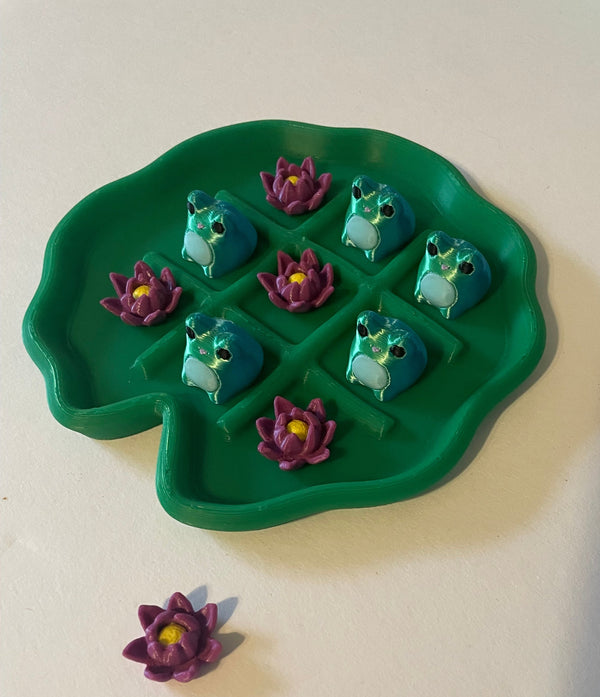 Green lily pad with frog and water lily designs on a white surface.
