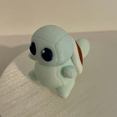 Handmade knitted-style 3D printed Pokémon-inspired water creature with textured filament, light blue body, large dark blue eyes, and brown turtle shell accents , photographed from the side on a white background.