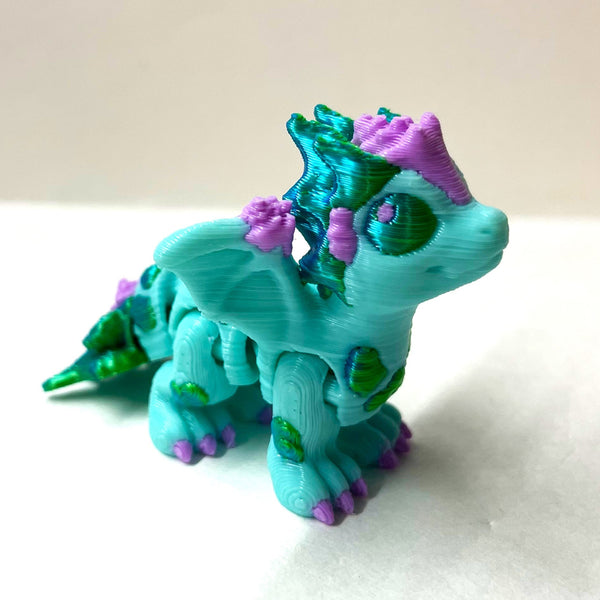 Toy dragon figure with lavender shell accents and blue/green kelp accents on a white surface.